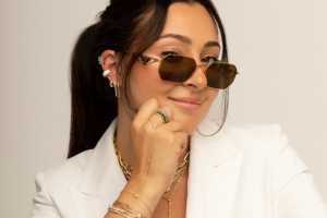 Woman in white blazer, wearing sunglasses and jewelry, smiles confidently. Text at the top reads “lena gianna jewelry.”