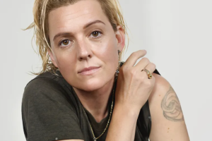 Person with short, light hair wearing a dark t-shirt, showing a tattoo on their arm.