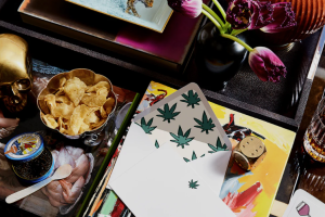A tabletop with playing cards featuring leaf designs, a bowl of chips, a decorative skull, and purple tulips in a vase.