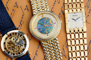 Three luxury watches on a brown scripted background: a skeleton watch with a dark strap, a colorful round watch, and a square gold watch with diamonds.