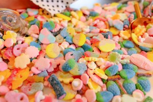 Assorted colorful candies scattered with a scoop and glass jar nearby.