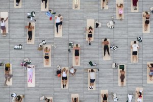 People lying on yoga mats in neat rows on a gray deck, viewed from above, some with bags beside them.