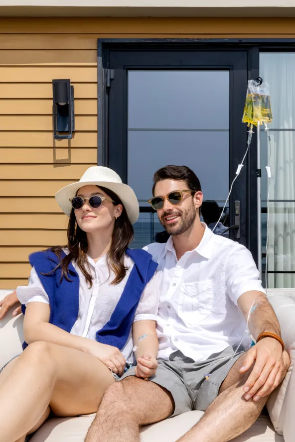 A couple lounges together outdoors while receiving saline IV drips.