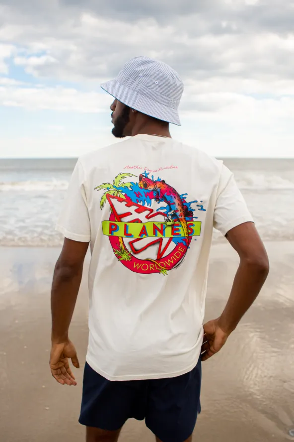 A man stands with his back toward the beach in a white t-shirt and bucket hat from Paper Planes.