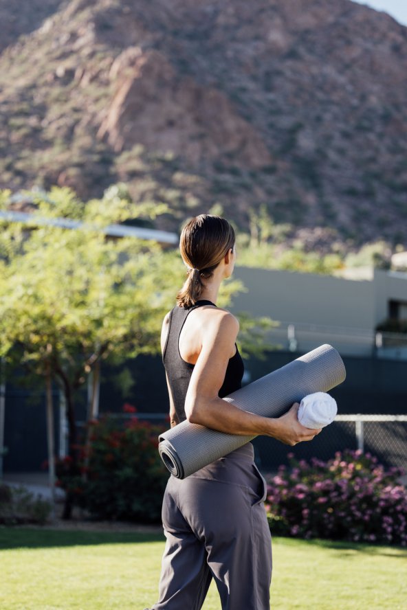 Woman in fitness attire with yoga mat walking on Sanctuary's Spa Fitness Lawn.