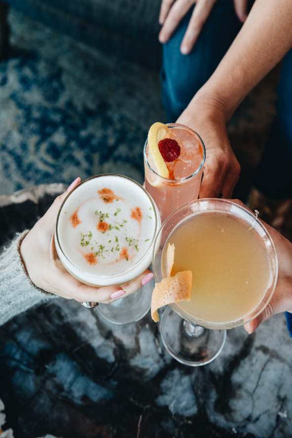 Three hands holding brightly colored cocktails in a cheers