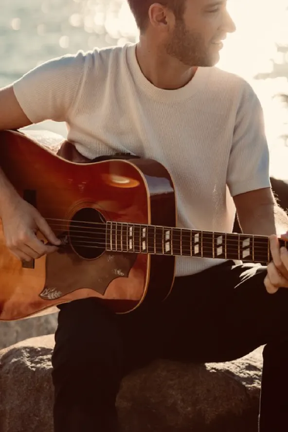 A closeup of a man holding a guitar with water in the background