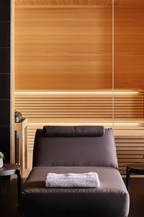 Three gray lounge chairs lined up with the sauna in the background at the Seawater Spa BathHouse