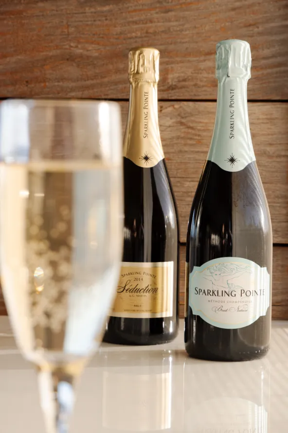 A glass of sparkling wine in the foreground and two bottles of Sparkling Pointe wine in the background