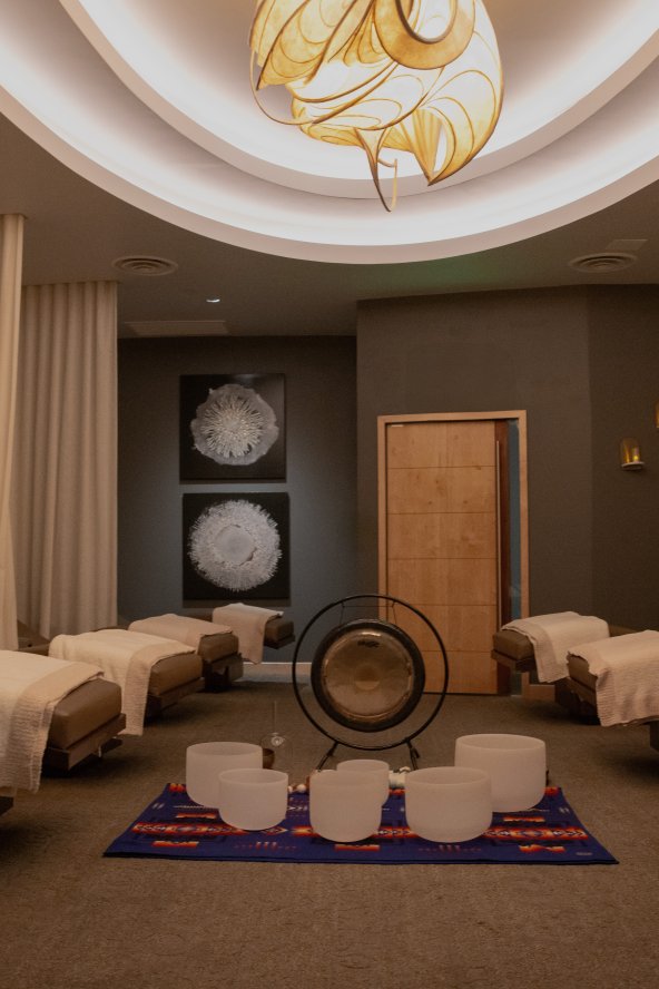 Spa relaxation room with several lounge chairs draped in white towels, warm lighting, and decorative artwork on the walls.