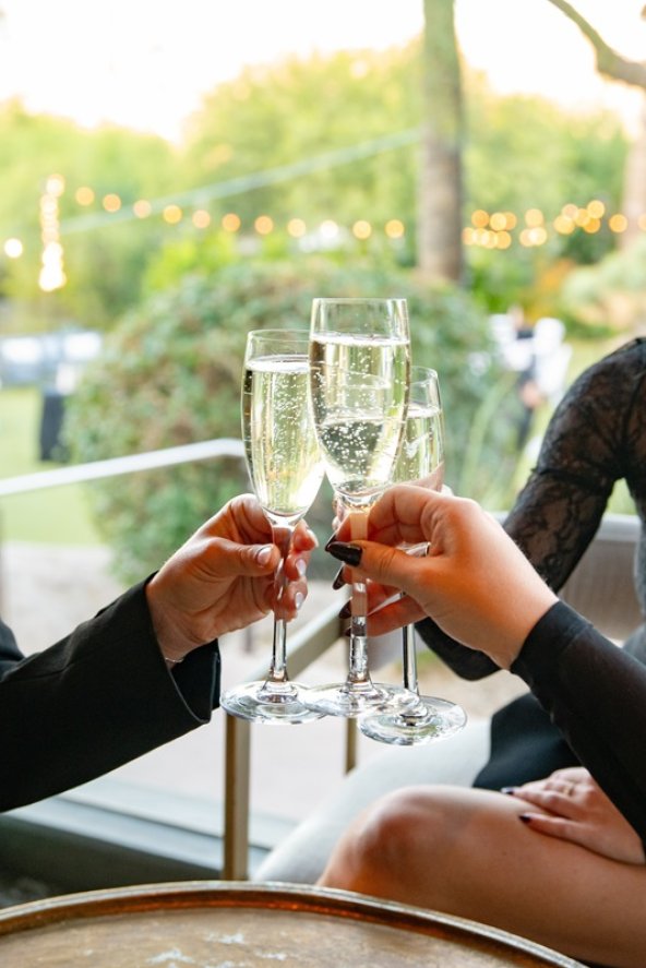 Women smiling and clinking champagne glasses in a festive outdoor setting.