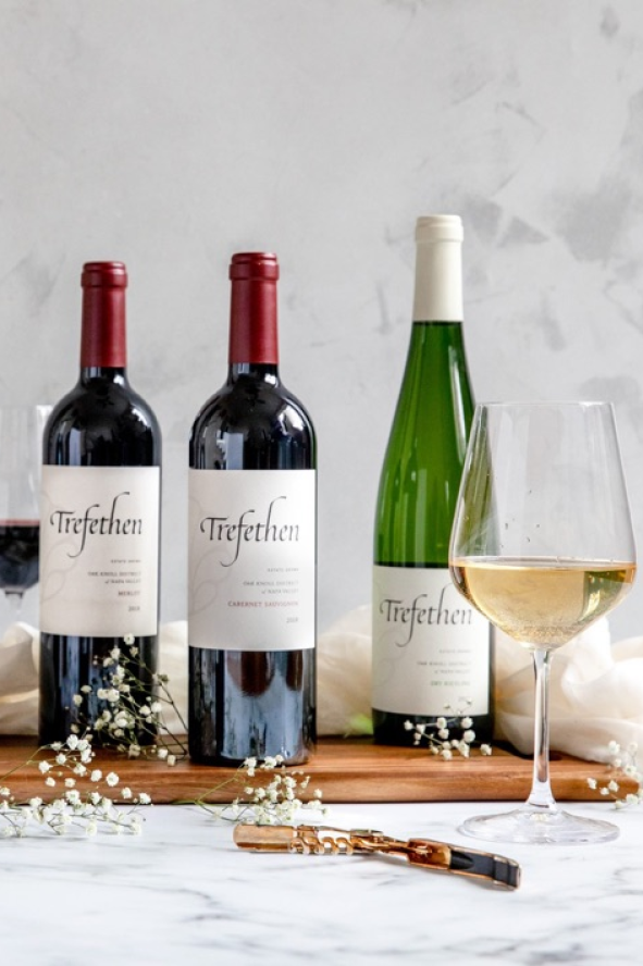 Bottles of wine with labels, accompanied by glasses of white and red wine, set on a marble table with delicate decorations.