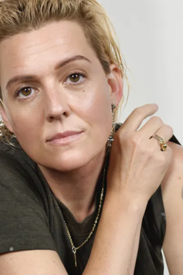 Person with short, light hair wearing a dark t-shirt, showing a tattoo on their arm.