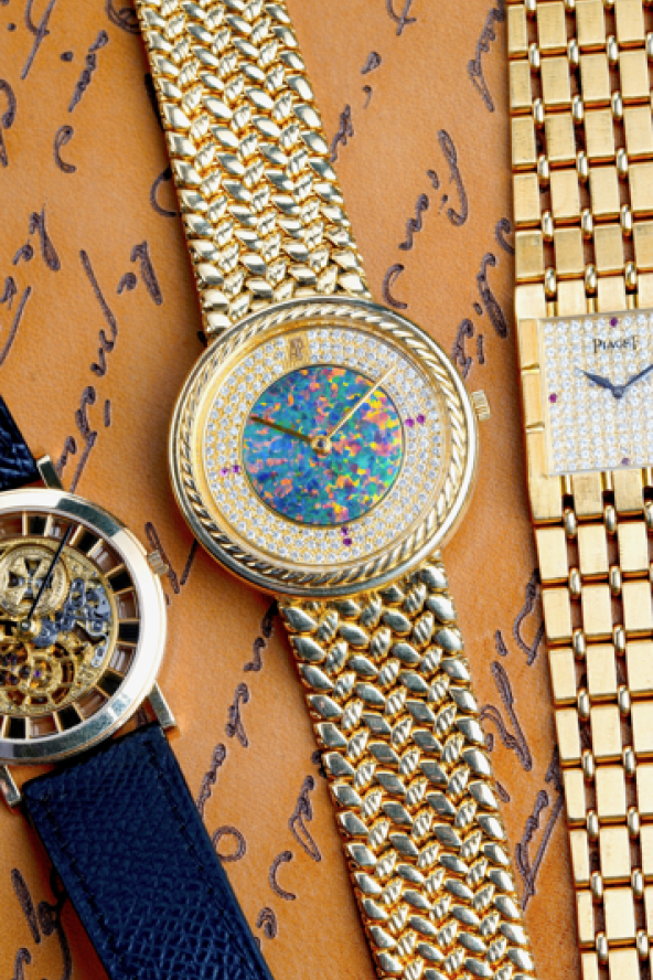 Three luxury watches on a brown scripted background: a skeleton watch with a dark strap, a colorful round watch, and a square gold watch with diamonds.