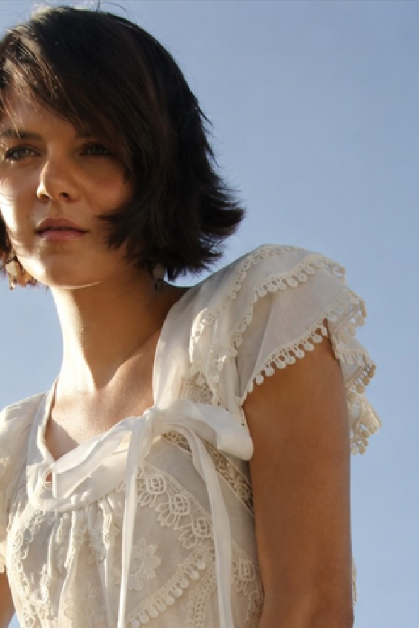 Young woman with short hair in a white dress against a clear blue sky, looking thoughtfully into the distance.