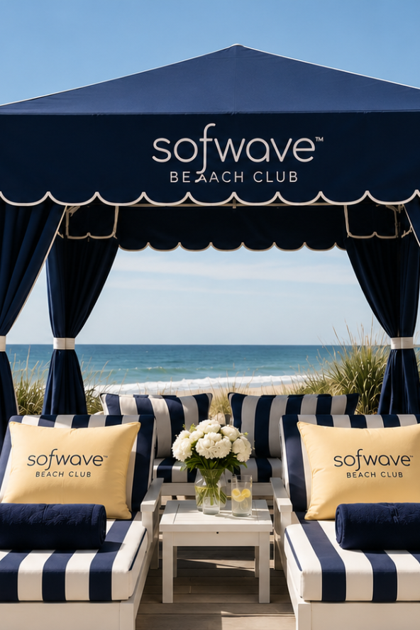 Beach cabana with striped lounge chairs, blue canopy reads "softwave BEACH CLUB," bag and surfboard nearby, ocean and dunes in the background.