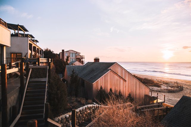 Coastal houses on a hillside overlook the ocean at sunset, with warm light illuminating the scene.