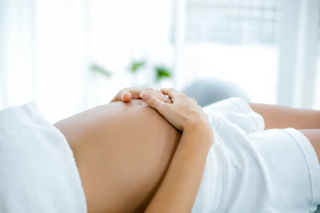 Pregnant woman holding belly and relaxing on spa table.