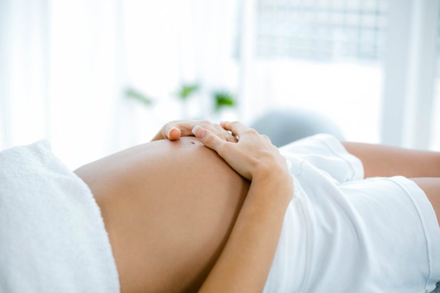 Pregnant woman holding belly and relaxing on spa table.