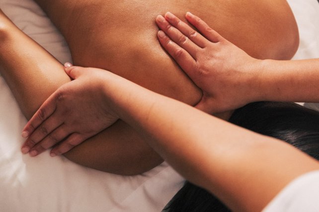 Woman with black hair lying on massage table getting neck and back massaged.