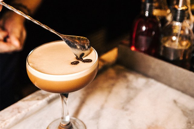 A bartender places a garnish on top of an espresso martini cocktail