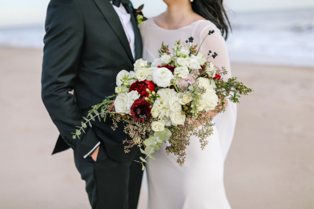 A groom and bride holding a bouquet stand on a beach
