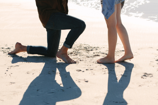 A man kneels before a woman on a beach