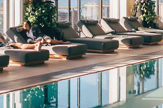 A woman relaxes on a lounge chair by the indoor pool.