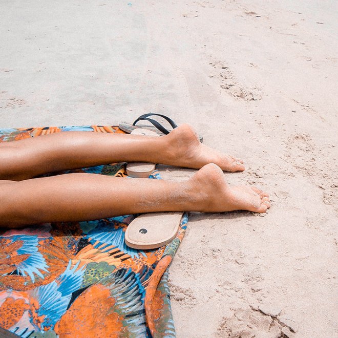 Bare legs stretched out on a beach, resting on a colorful towel.