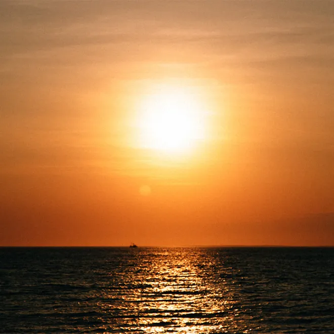 A serene ocean view at sunset with a bright sun and calm waters.