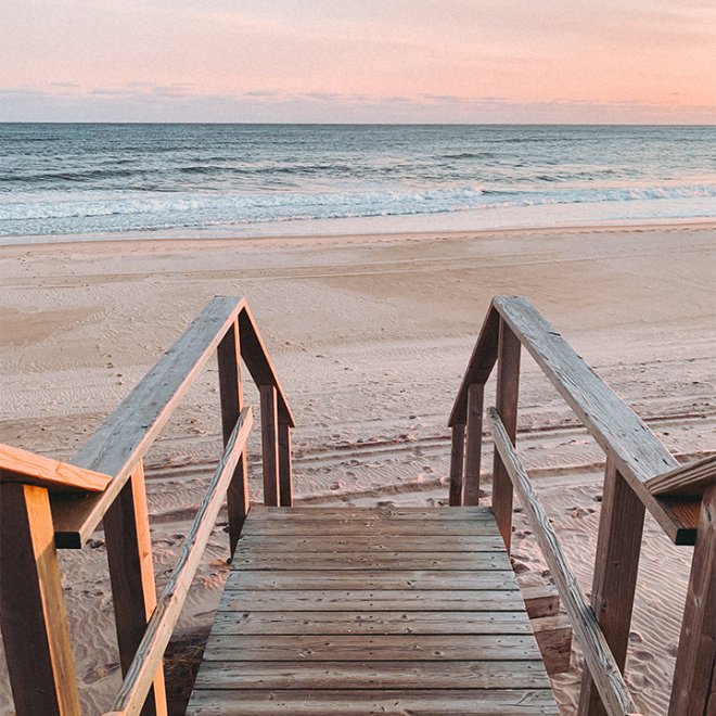 Stairs leading to the beach pink sky at sunset