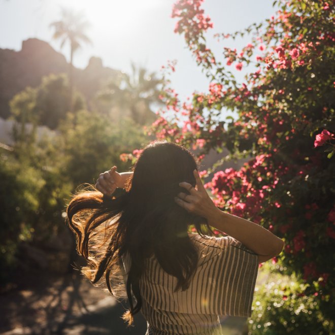 Woman letting her hair down as the sun shines through the lush desert setting.