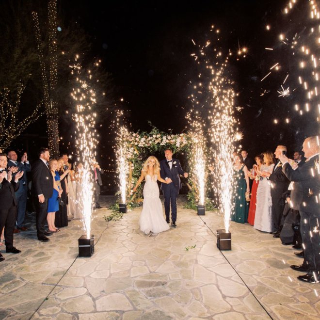 Couple walking down the aisle as sparklers shoot around them.