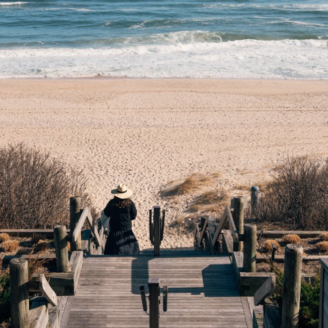 Woman walking down wooden path to beach.