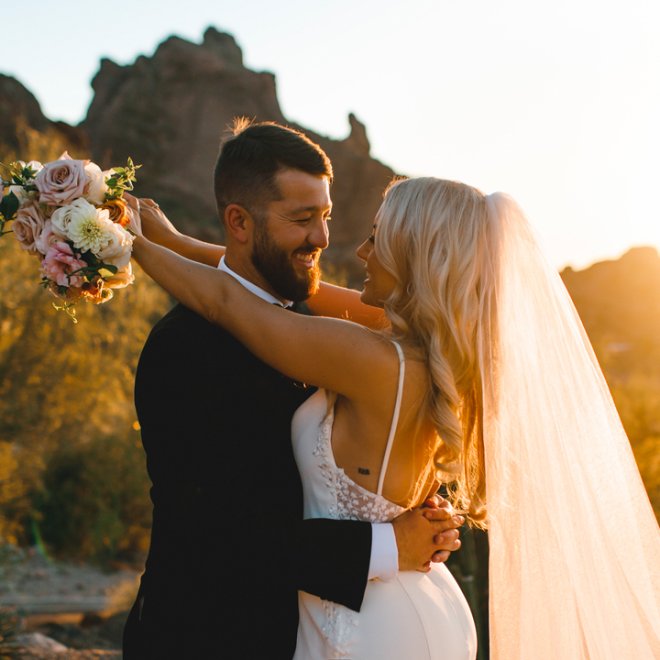 Bride and groom embracing with sun setting over Praying Monk in background.