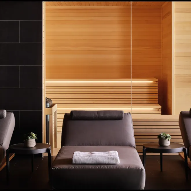 Three gray lounge chairs lined up with the sauna in the background at the Seawater Spa BathHouse