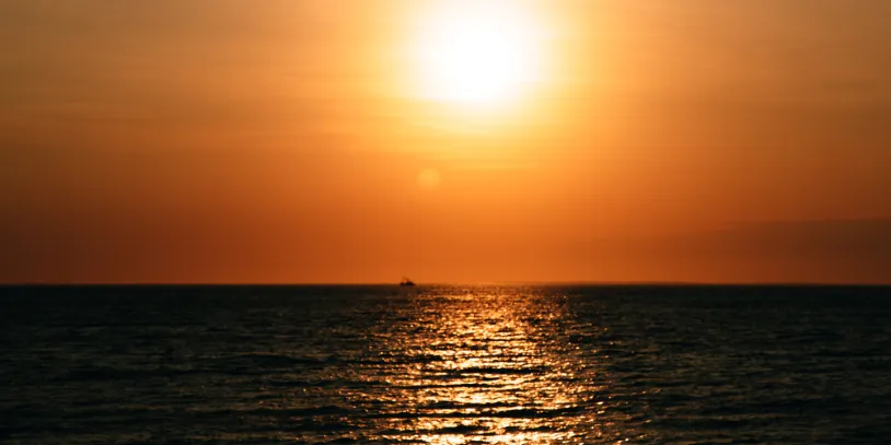 Sunset over the ocean with a glowing orange sky and shimmering reflections on the water.