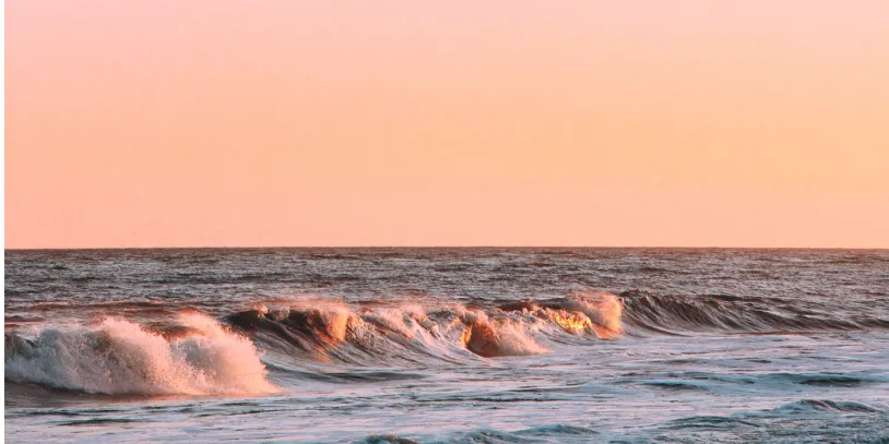 Waves rolling in at sunset with an orange sky.