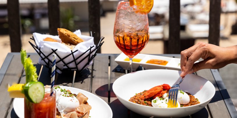 Hand with fork digging into brunch spread outdoor at Scarpetta Beach.