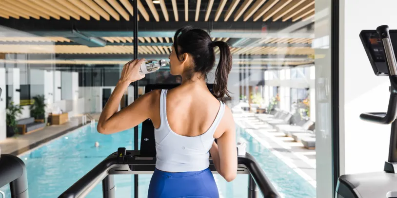 A woman on a treadmill in a gym with a pool in the background.