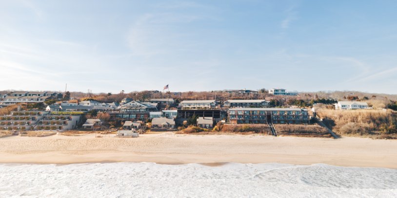 Drone shot of waves crashing on shoreline with Gurney's Montauk during fall.