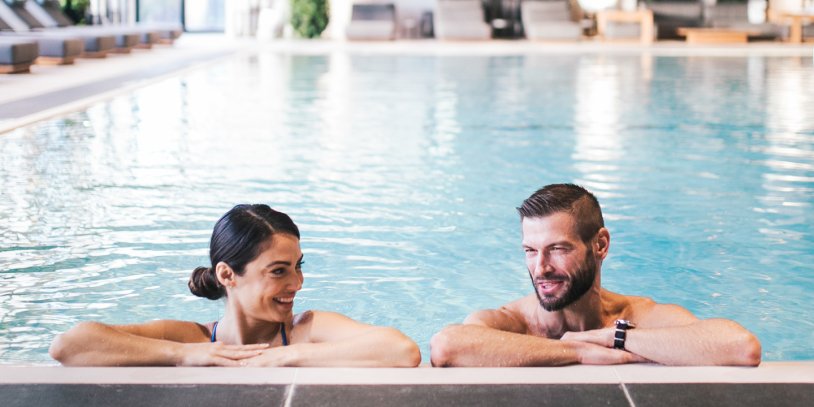 Couple smiling together and relaxing on pool ledge.