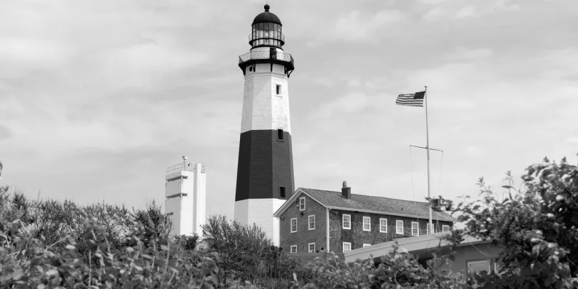 Black and white photo from across field of Montauk lighthouse and surrounding  buildings.