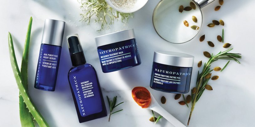 An array of Naturopathic skin products in blue packaging surrounded by fresh ingredients like aloe and collagen.