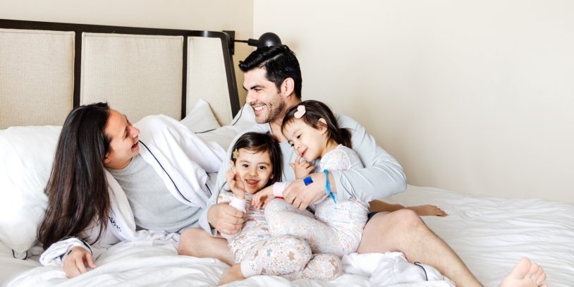 Husband and wife laughing in bed while cuddling with their two young daughters.