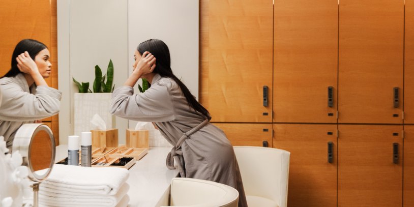 Woman applying skin care product in spa locker room mirror after a treatment.