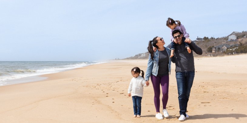 Husband and wife walking along beach and laughing with two daughters.