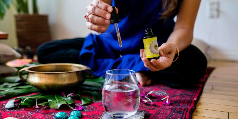 Woman in blue adding drops LOTUSWEI drops to glass of water while sitting.