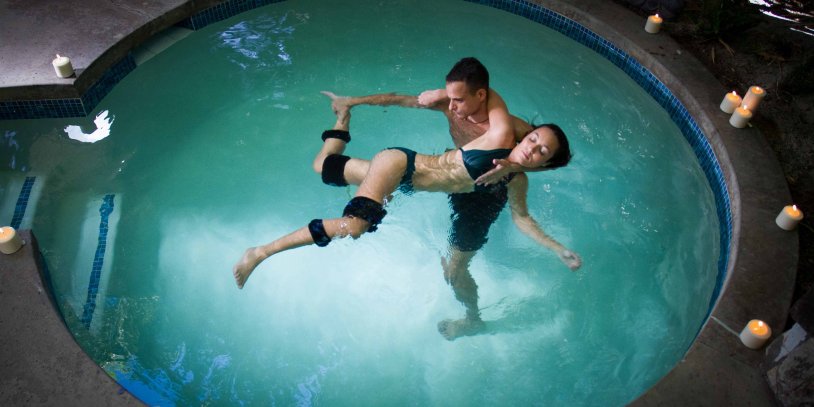 Woman receiving aquatic watsu treatment with therapist in candle lit private pool.