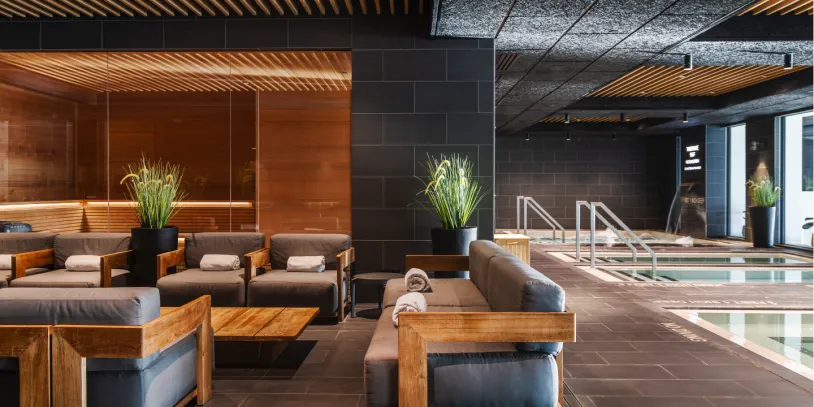 A seating area with sofas and a coffee table in a spa with a pool in the background.